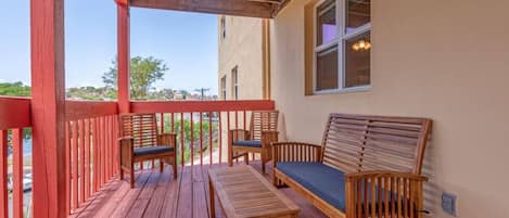 Una terraza de madera con barandilla roja, un banco y dos sillas.