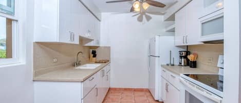 Una cocina compacta con armarios blancos, un lavamanos, una estufa y un ventilador de techo.