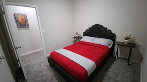 Ein Schlafzimmer mit einem Bett, einer Tür, einem kleinen Tisch und einem an der Wand hängenden Gemälde.