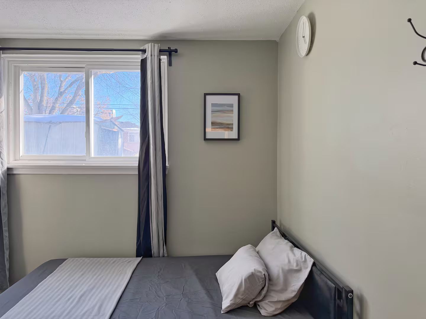 Una camera da letto con un letto, una finestra con tende, una sveglia a muro e un quadro incorniciato.