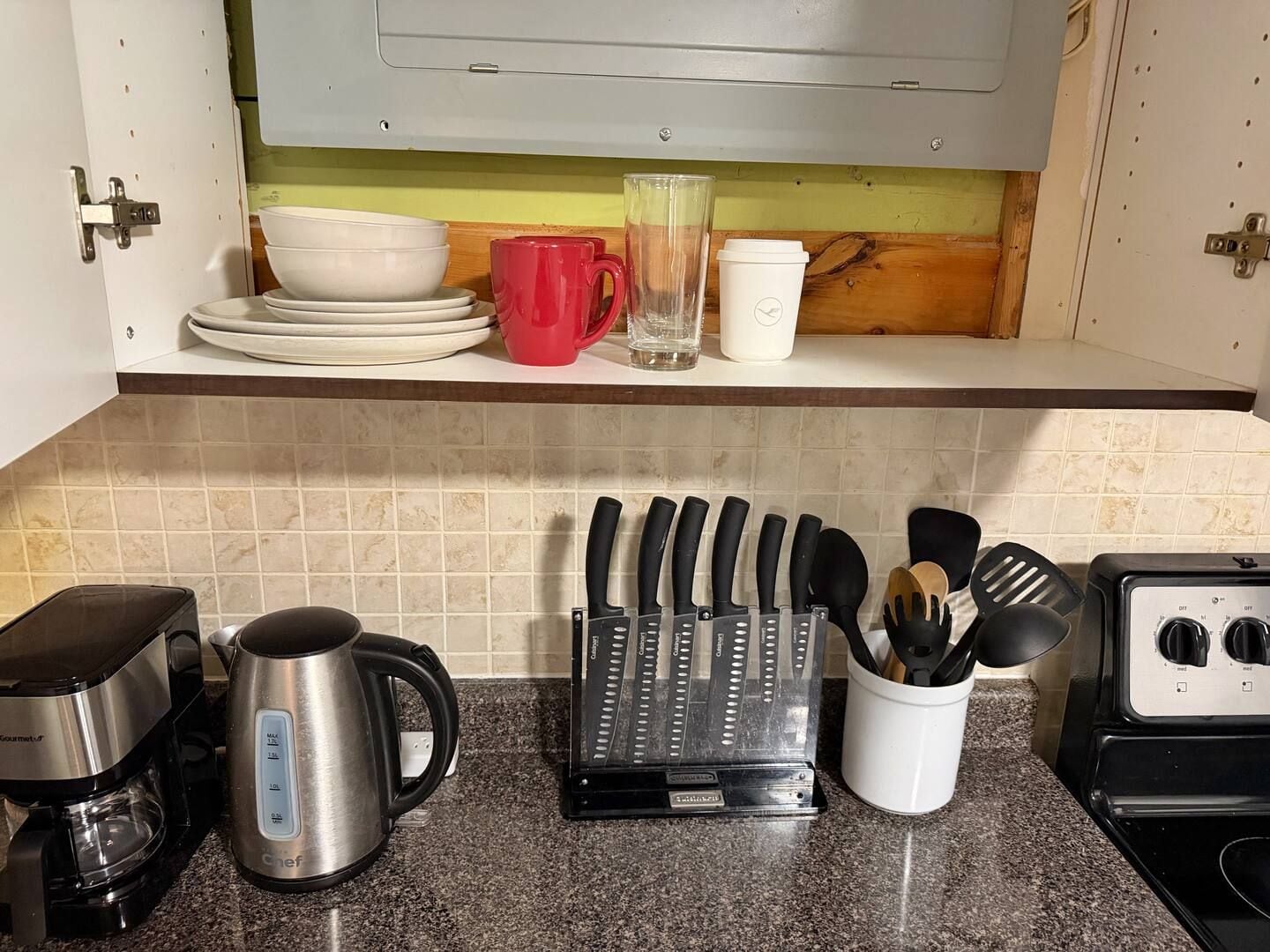 A kitchen counter with a coffee maker, a kettle, a knife block, and a cup holder.