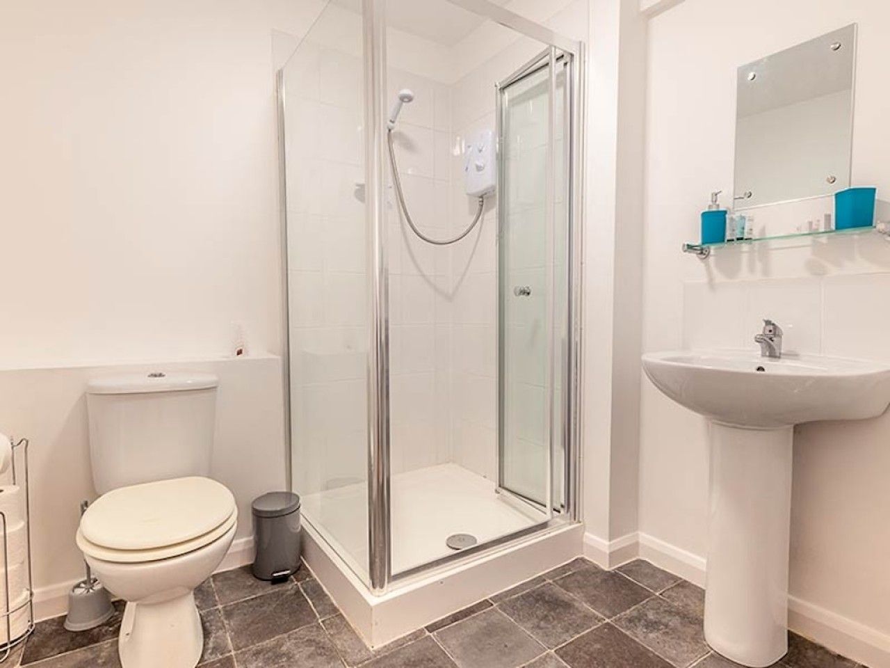 Een badkamer met een douchecabine, toilet en een wastafel op een zuil.