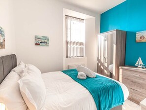 A hotel room with a bed, a window with blinds, a wardrobe, and a small table with a decorative item. - Private Beach-Front Apartment on the English Riviera with outdoor courtyard (Paignton)