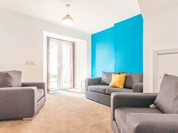 Een woonkamer met een grijze zithoek, een blauwe accentmuur en een schuifdeur naar een buitenruimte.