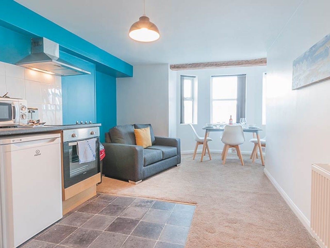 A compact living space with a kitchenette, a sofa, a dining area, and a window providing natural light.