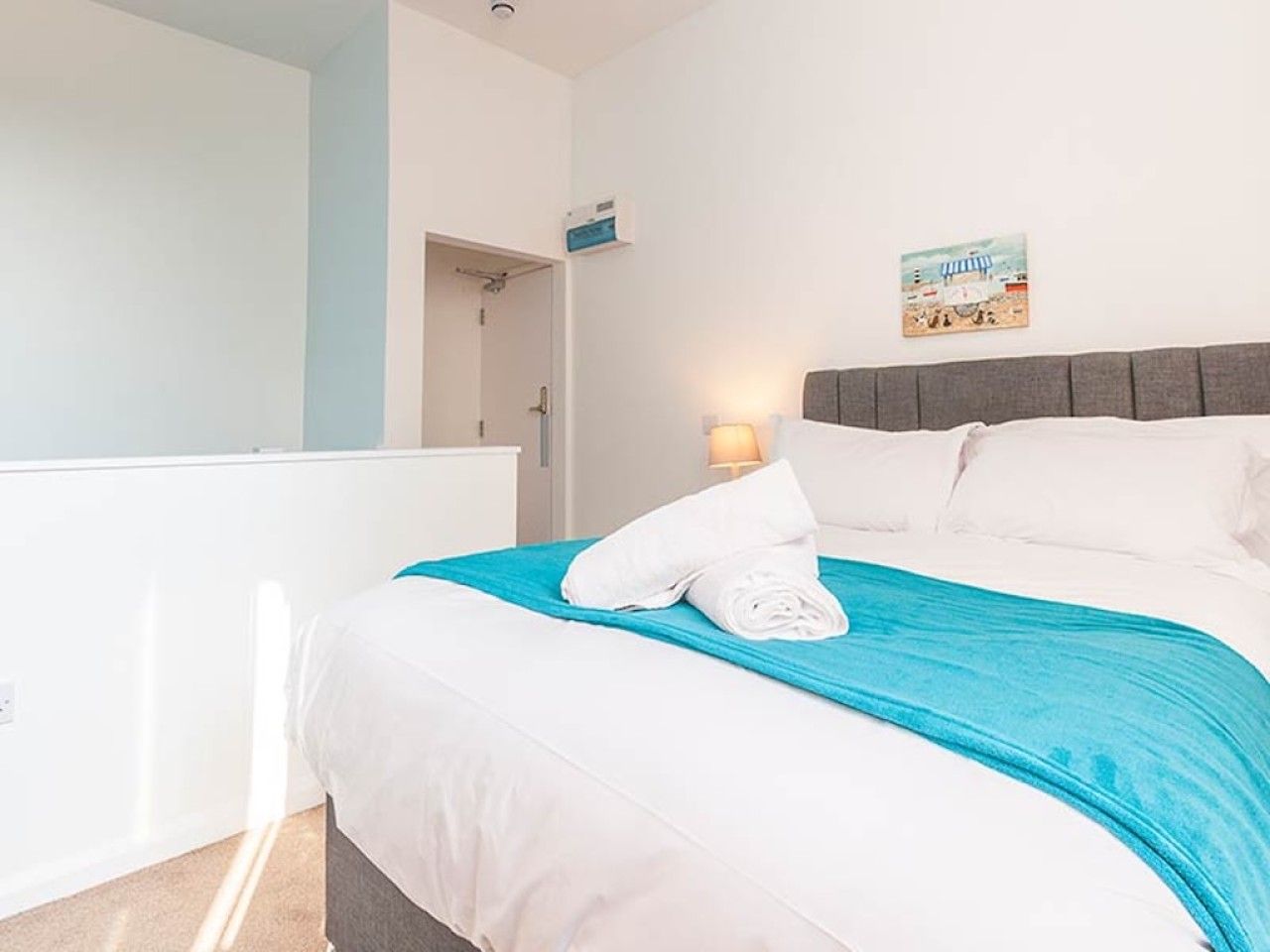 A hotel room with a bed, a nightstand, a wall-mounted lamp, and a painting.