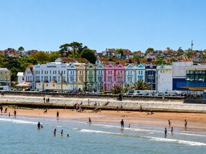 A beachfront hotel with colorful buildings, a sandy beach, and a clear sky. - Private Beach-Front Apartment on the English Riviera with outdoor courtyard (Paignton)