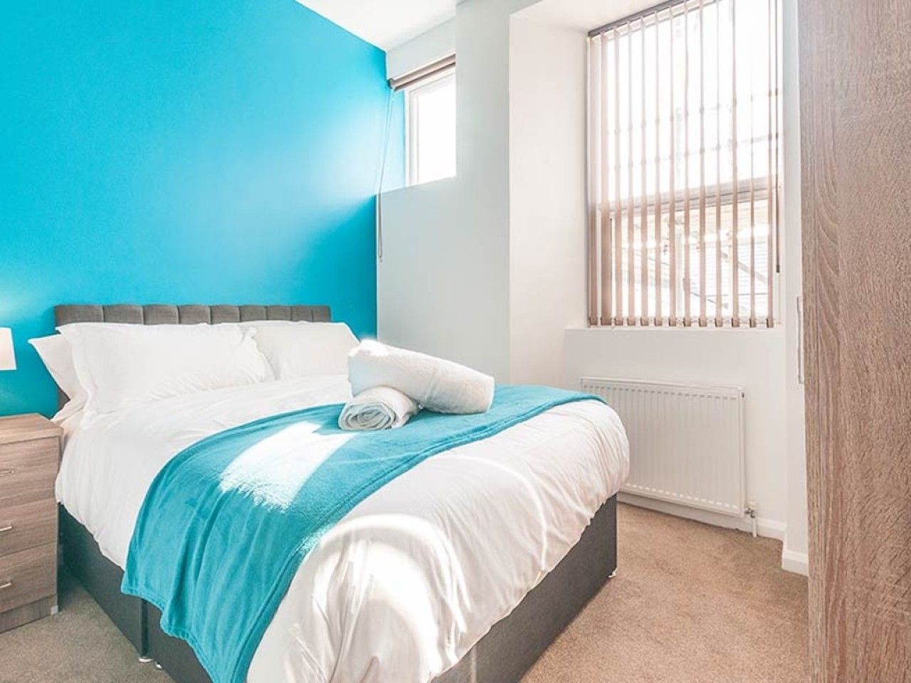 Un dormitorio con cama, una mesita de noche, una ventana con persianas y un radiador.