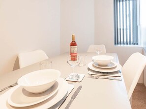 A dining table set for four with white plates, bowls, cutlery, and a bottle of red wine. - Private Beach-Front Apartment on the English Riviera with outdoor courtyard (Paignton)