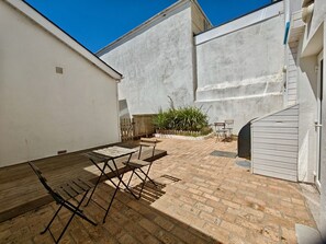 An outdoor patio area with a wooden table and chairs, a brick floor, and a white wall. - Private Beach-Front Apartment on the English Riviera with outdoor courtyard (Paignton)
