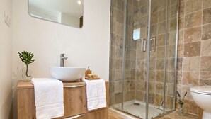 Un baño moderno con cabina de ducha de vidrio, tocador de madera con lavabo integrado y retrete.