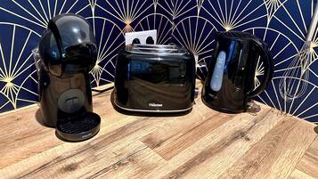 A coffee maker, a toaster, and a mug on a wooden table with a geometric patterned wall in the background.