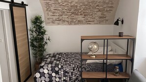 Una habitación compacta con cama, escritorio, silla, sofá, un globo terráqueo y una planta.