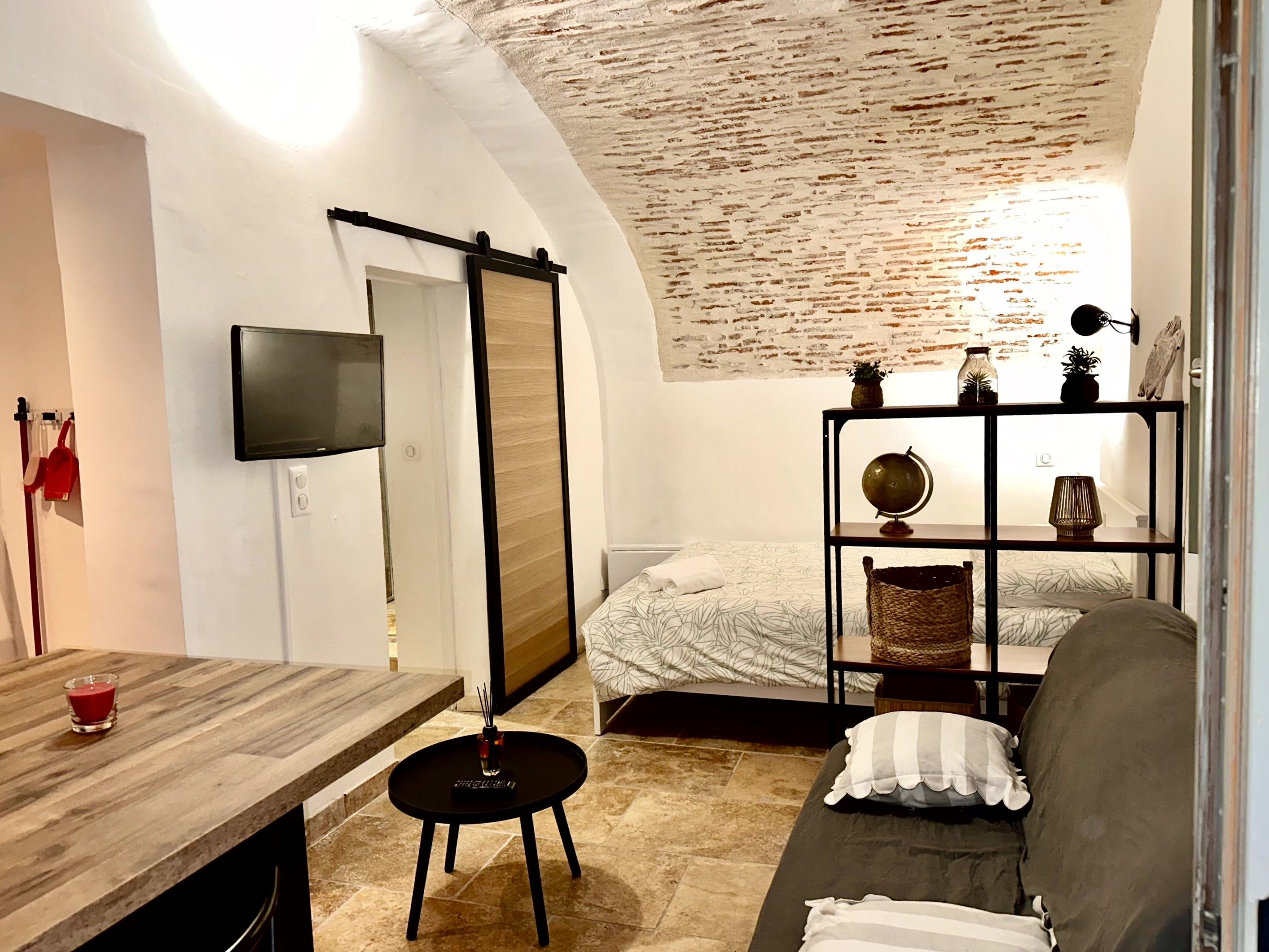 Een kleine kamer met een bed, een bank, een tafeltje en een aan de muur bevestigde televisie.