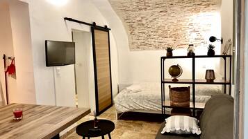 Een kleine kamer met een bed, een bank, een tafeltje en een aan de muur bevestigde televisie.
