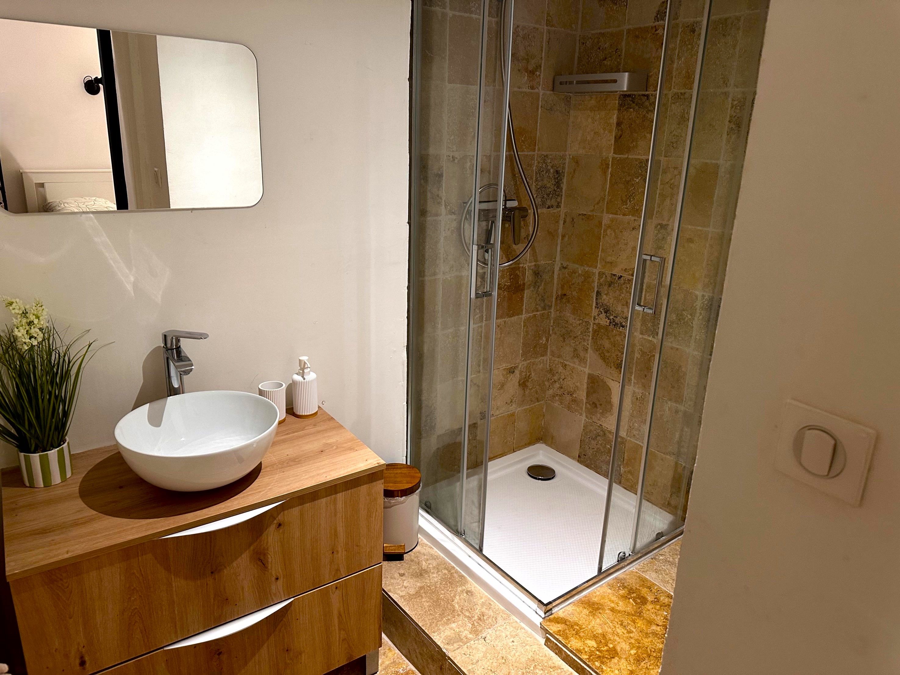 Ein Badezimmer mit einem Holzausziehtisch, einem weißen Waschbecken und einer Duschkabine.