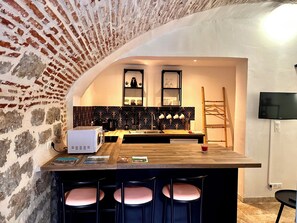 Una cocina con pared de ladrillo, microondas, cafetera y mostrador de madera con taburetes de bar.