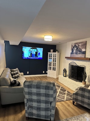 Ein Wohnzimmer mit Fernseher, Kamin, einer Couch und einem Sessel.