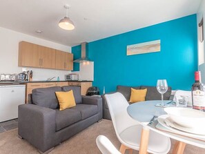 A compact living space with a kitchenette, a dining area, and a sofa with cushions. - Private Beach-Front Apartment on the English Riviera with free, private parking (Paignton)