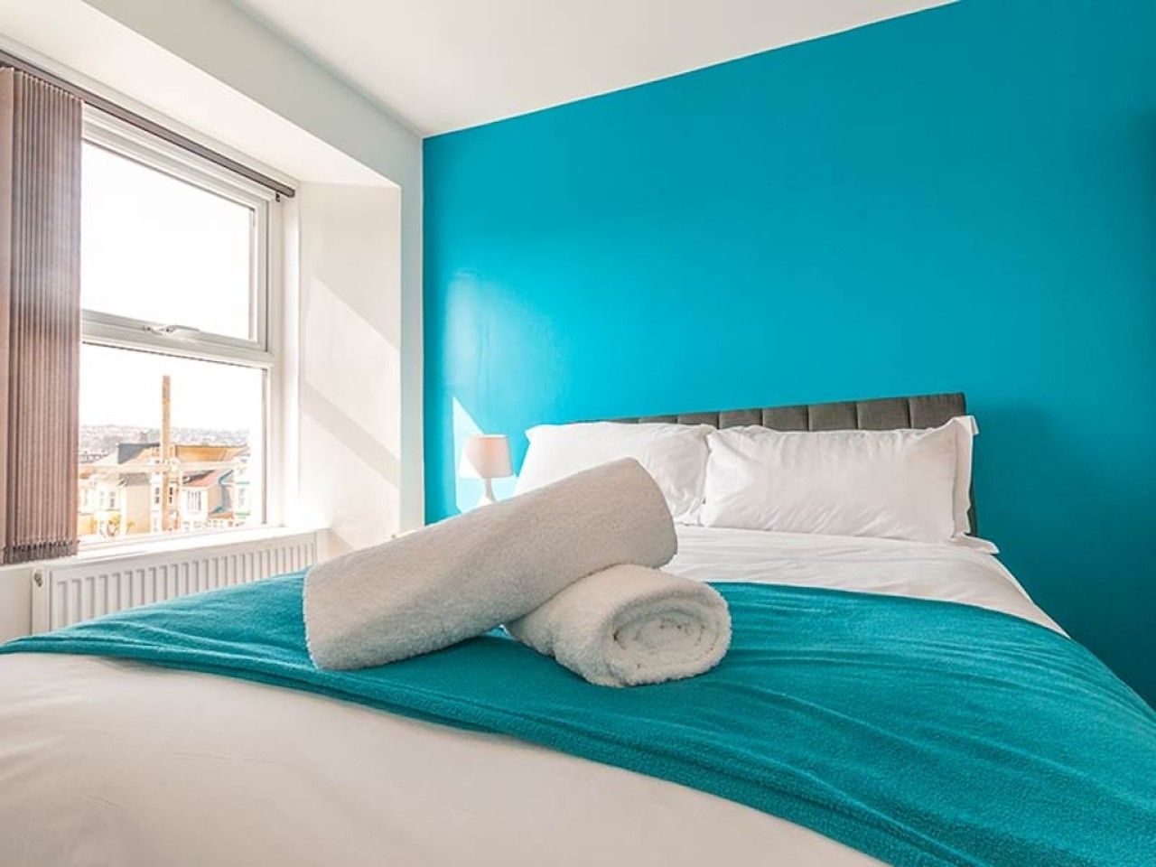 A hotel room with a bed, a window, and a view of the city.
