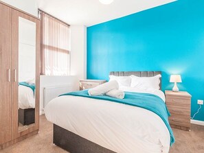 A bedroom with a bed, a nightstand, a lamp, a wardrobe, and a window with curtains. - Private Beach-Front Apartment on the English Riviera with free, private parking (Paignton)