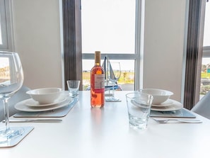Una mesa de comedor dispuesta con platos, tazones y vasos blancos, una botella de licor y una copa de vino.
