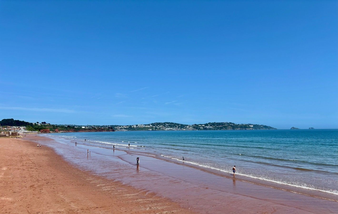 A beach with a clear sky, calm sea, and distant hills.
