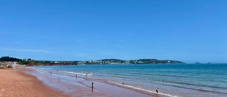 A beach with a clear sky, calm sea, and distant hills.