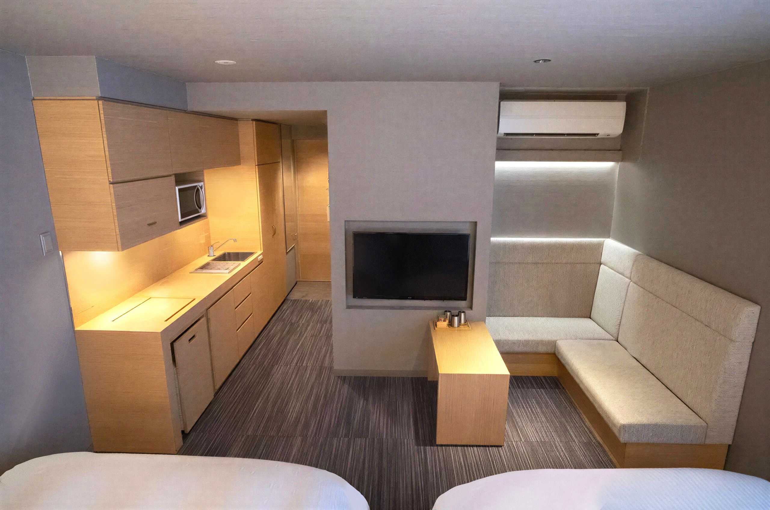 Quarto de hotel compacto com cozinha compacta, televisão de tela plana, sofá e duas camas.