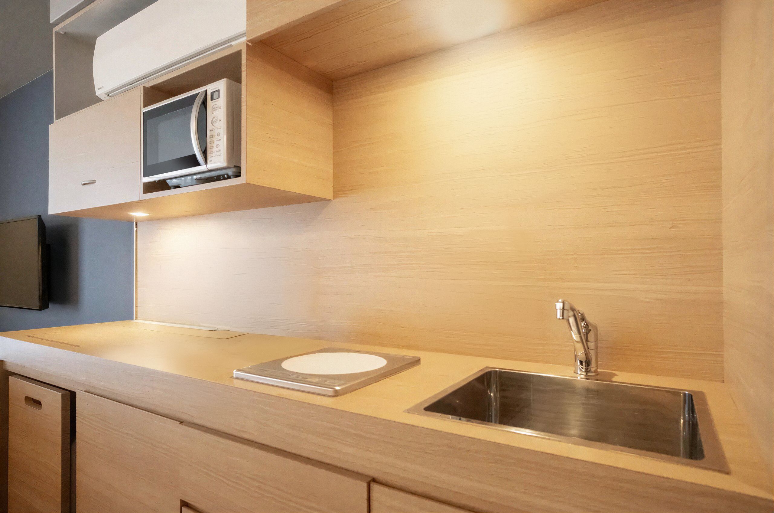 Una cocina moderna con microondas integrado, un lavamanos de acero inoxidable y muebles de madera.