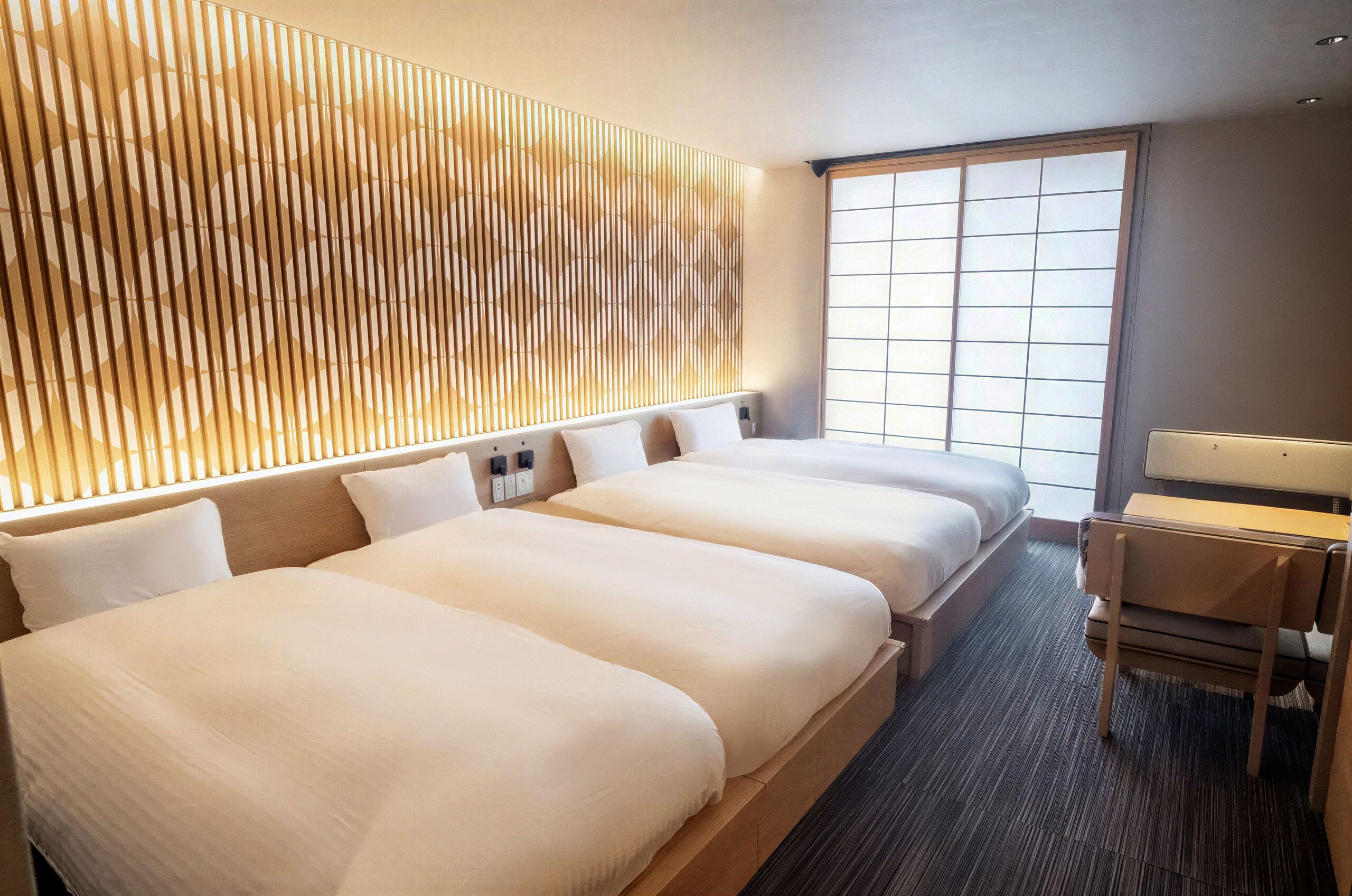 A hotel room with two beds, a desk, and a large window.