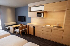 Ein Hotelzimmer mit Bett, Schreibtisch, Stuhl, Mikrowelle, Fernseher und einer kleinen Küchenzeile.