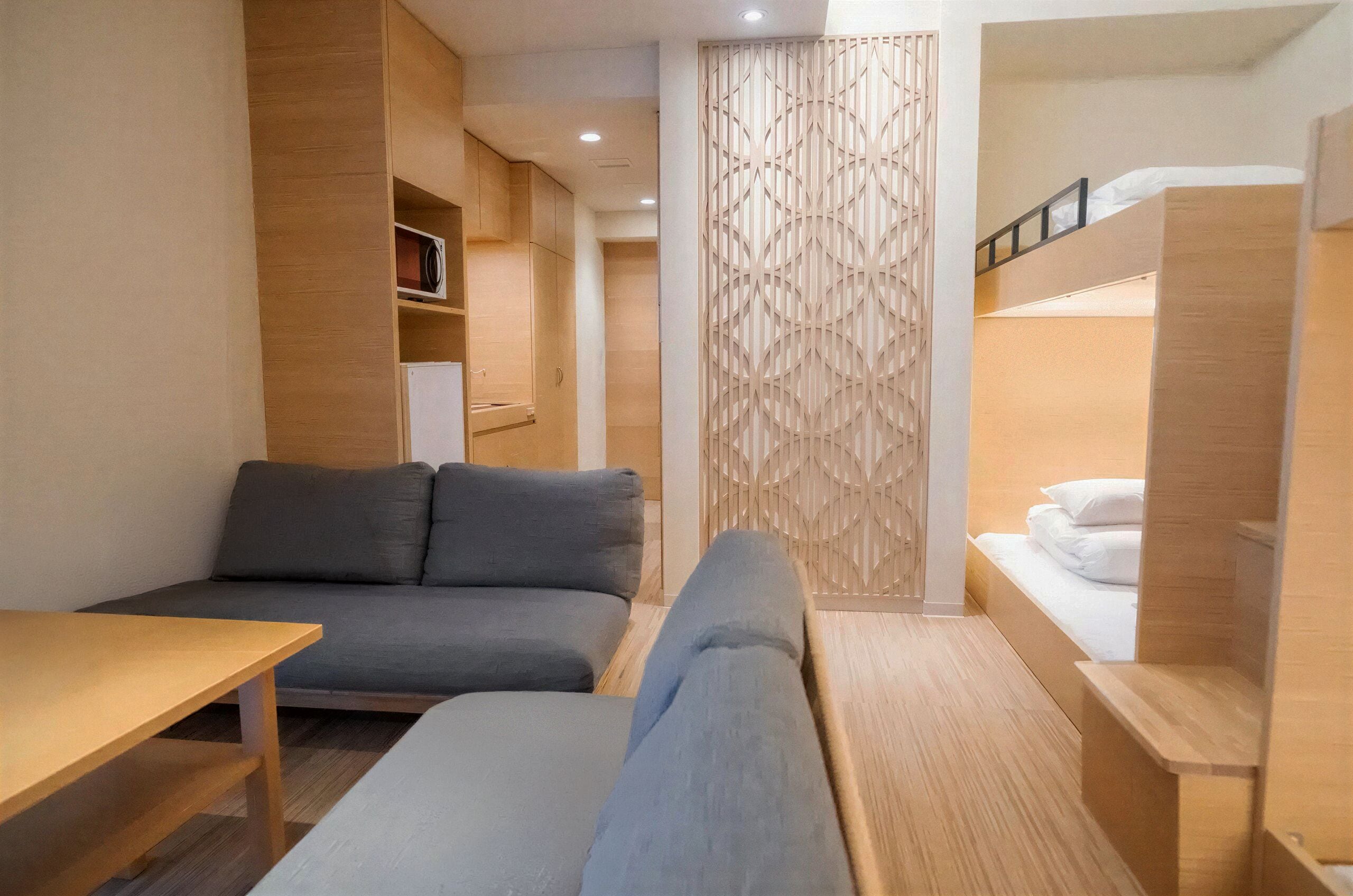 Habitación de hotel compacta con sofá, una mesita, una litera y un separador decorativo.