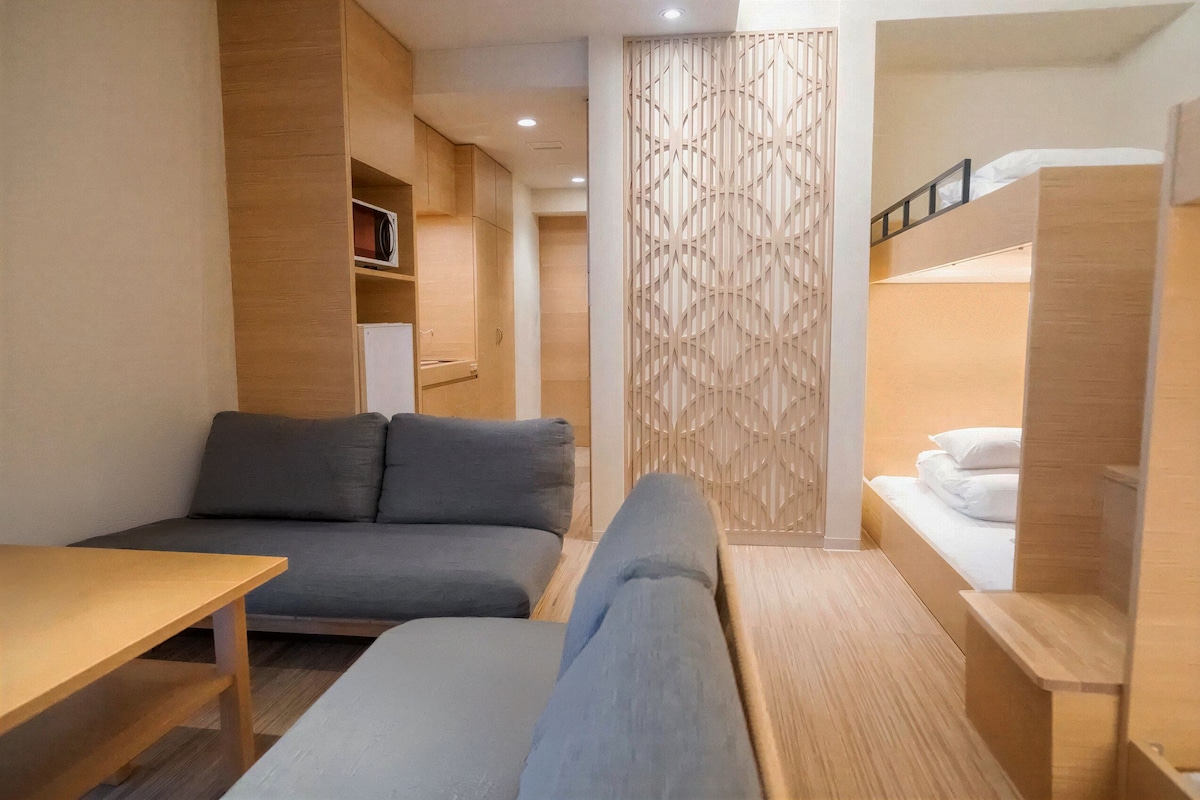 A compact hotel room with a sofa, a small table, a bunk bed, and a decorative partition.