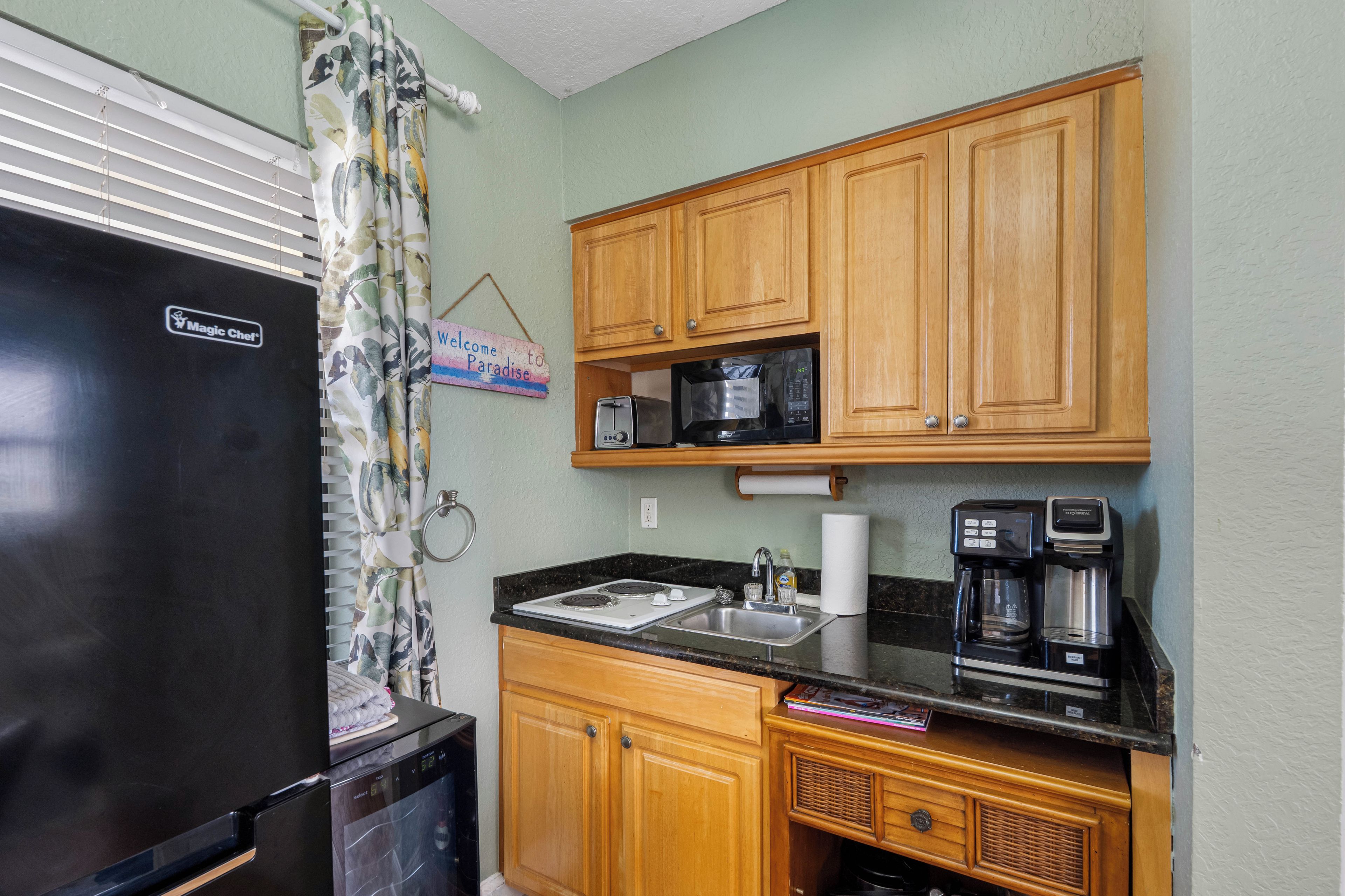 A compact kitchen with a refrigerator, microwave, coffee maker, and wooden cabinets.