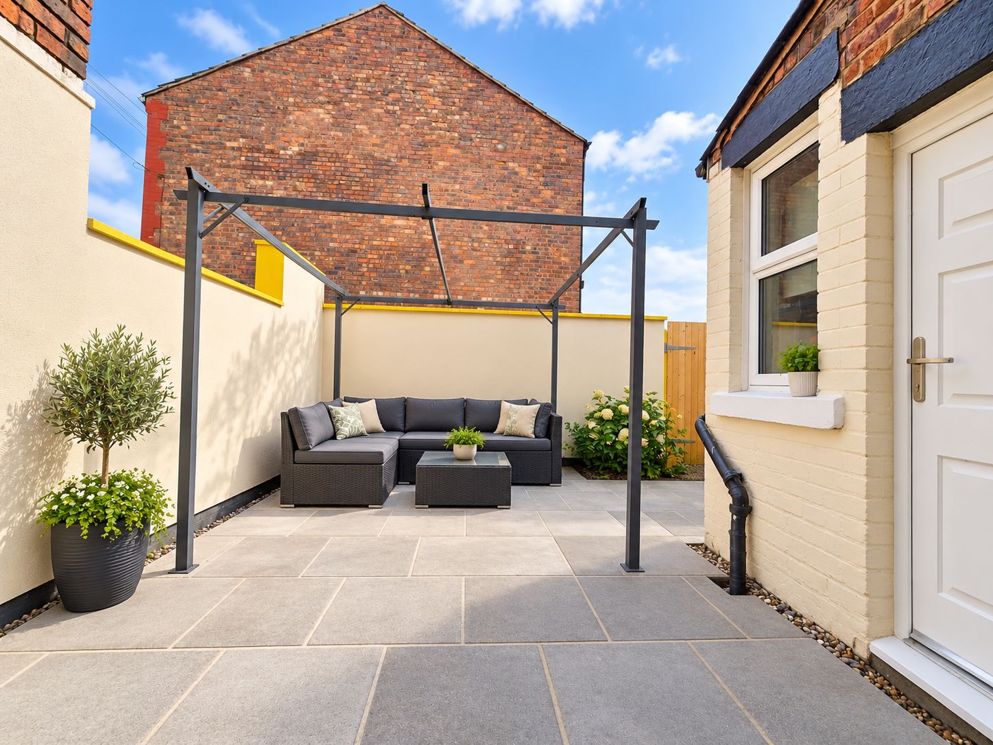 A patio with a black metal pergola, a grey sofa set, and potted plants.