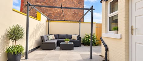 A patio with a black metal pergola, a grey sofa set, and potted plants.