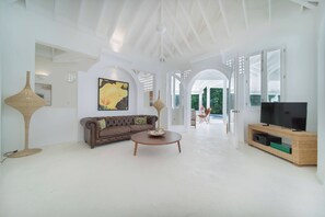 A spacious living room with a brown sofa, a coffee table, and a television on a woven stand. - Walk to beach. Luxury Mediterranean villa includes golf cart. (La Romana)