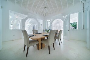 A dining area with a large table, four chairs, and a view of the outdoors through arched windows. - Walk to beach. Luxury Mediterranean villa includes golf cart. (La Romana)