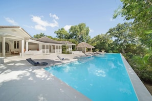 Un'area piscina con lettini, una zona relax coperta e una casa con tetto in tegole.