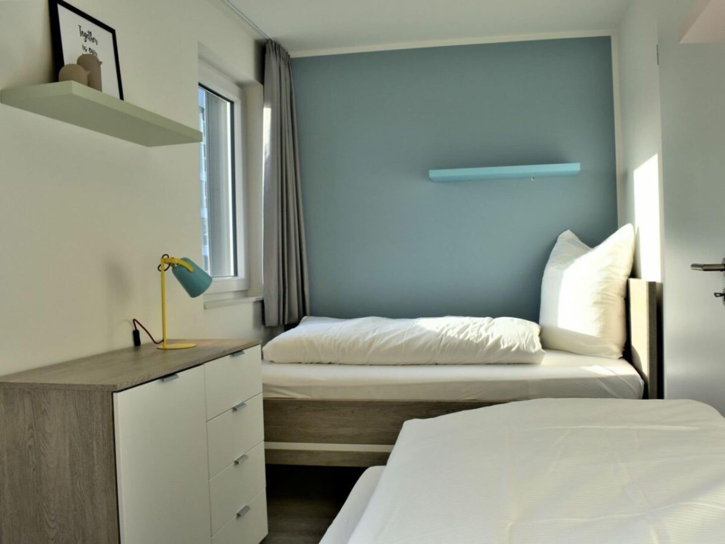 A bedroom with a bed, bedside table, lamp, and a wall-mounted shelf.