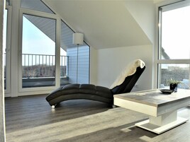A modern room with a curved black chair, a white table, and large windows offering a view of the outdoors.