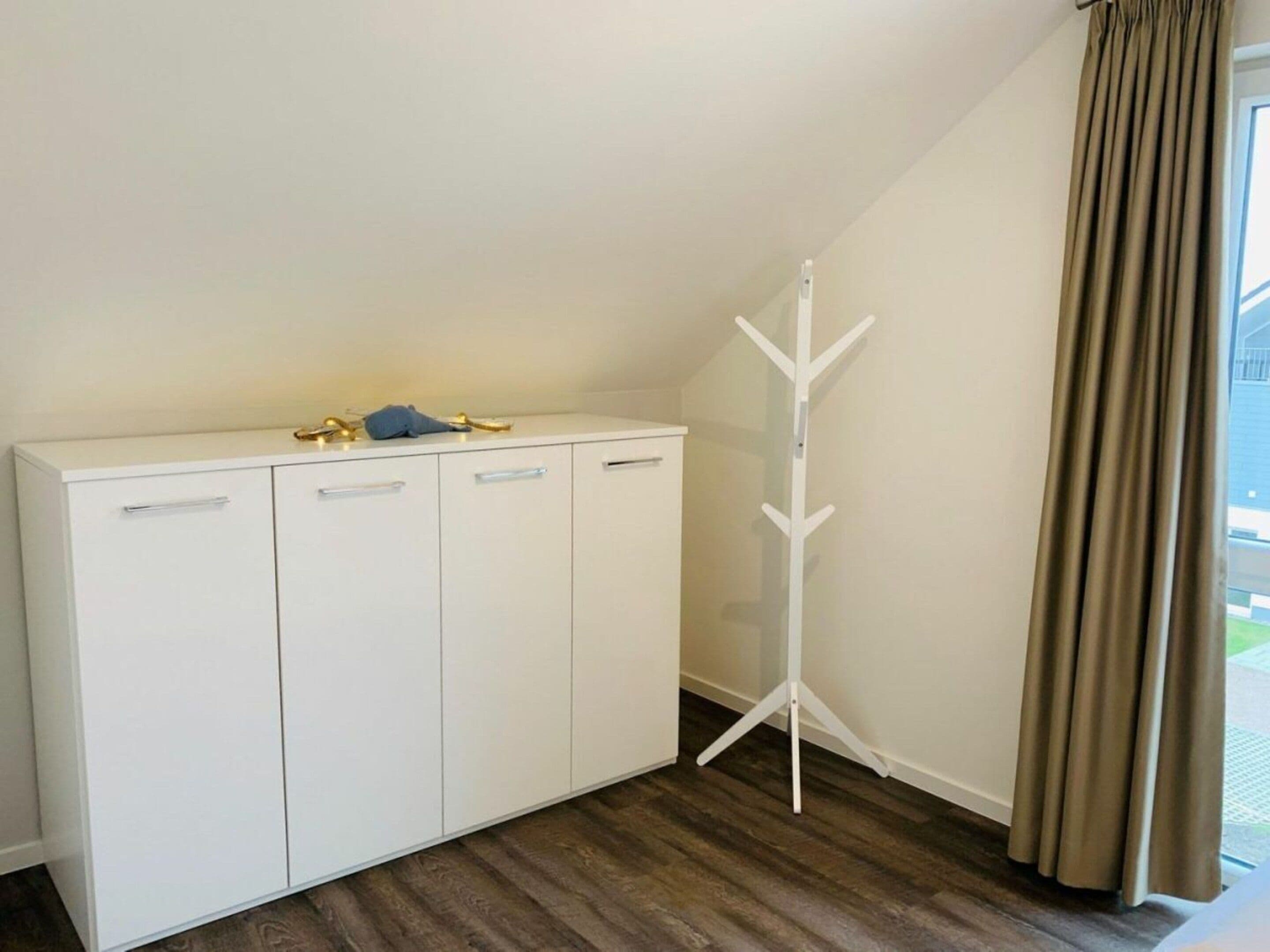Ein Zimmer mit einem weißen Schrank, einem Kleiderhaken und einem fenster mit Vorhängen.