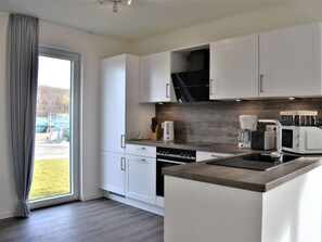 A modern kitchen with white cabinets, a built-in oven, a coffee maker, and a microwave. - House No. 16, Deichgraf (Wangerland)