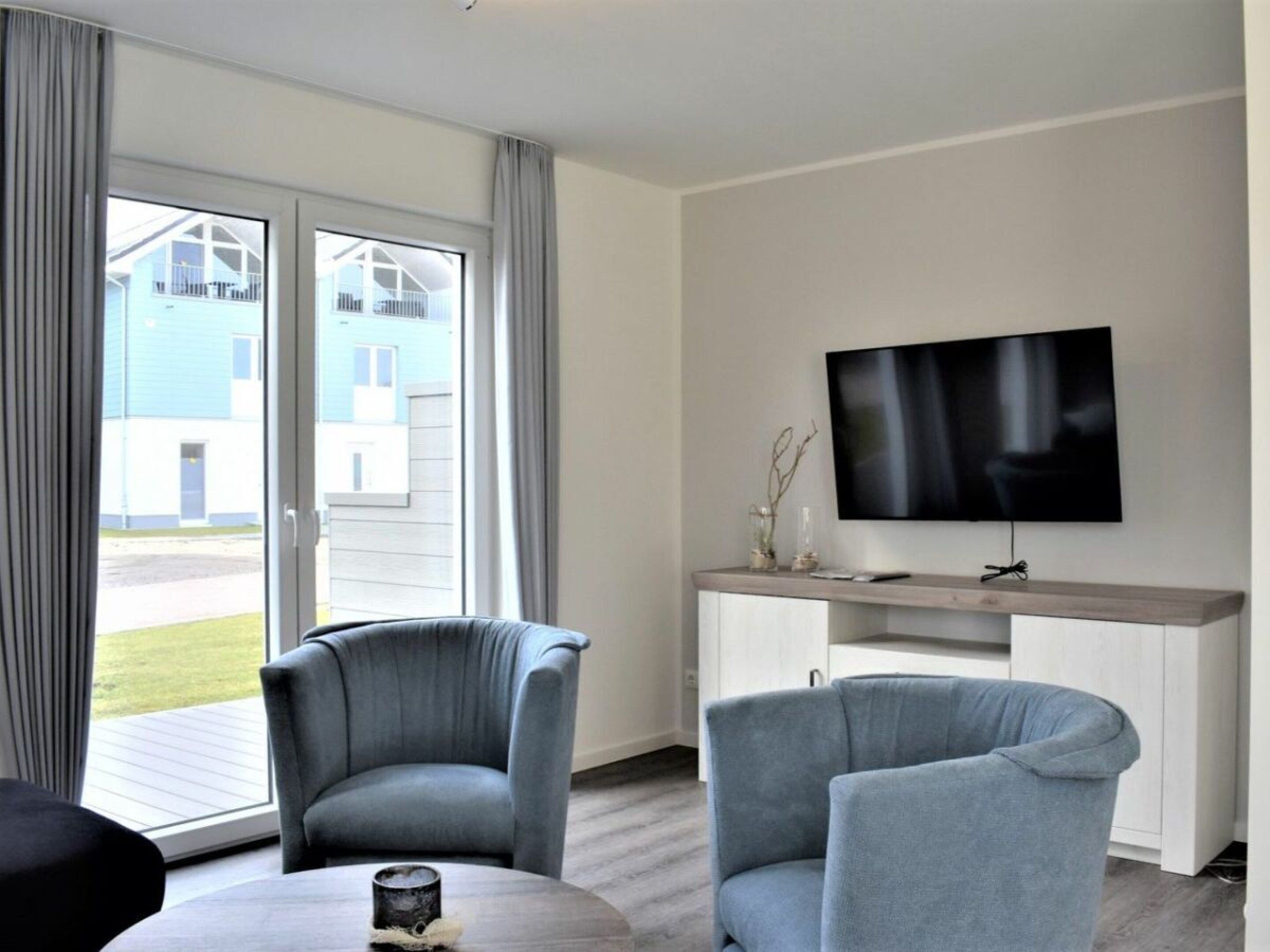 A modern living room with a flat-screen TV mounted on the wall, a grey sofa, and a coffee table.