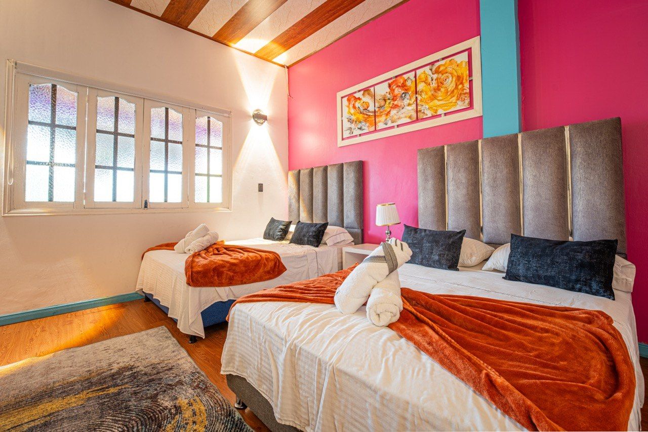 A hotel room with two beds, a large window, and a pink accent wall.