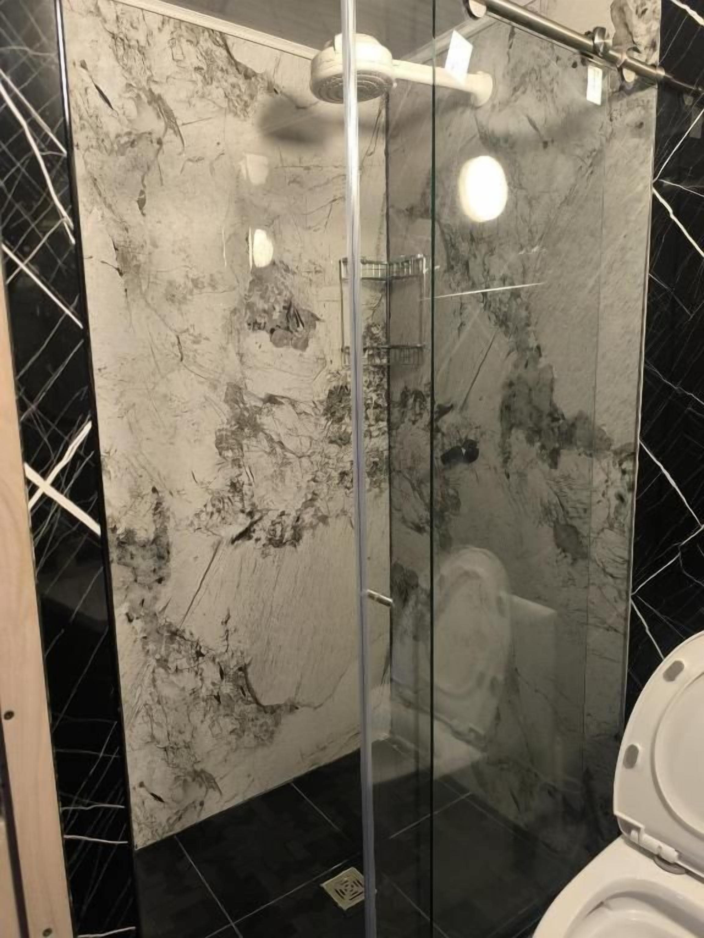 Cabina de ducha con paredes de mármol, ducha de mano y puerta de cristal.