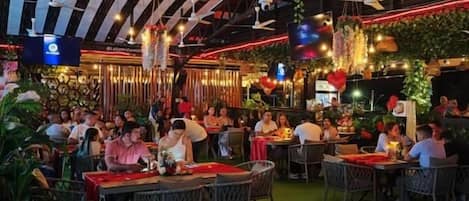 Un comedor interior con mesas y sillas, piso a cuadros y decoraciones colgantes.