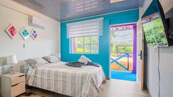 Quarto com cama, mesa de cabeceira, ar condicionado, janela com persianas e vista para área externa.