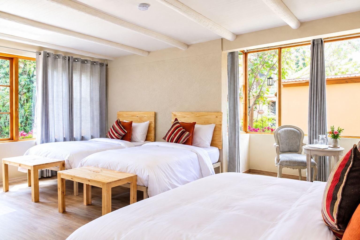 Une chambre d’hôtel avec deux lits, une table en bois, une chaise et une vue sur la verdure par les fenêtres.